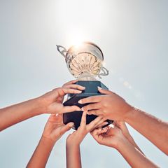 trophy cup being held high by 6 female hands