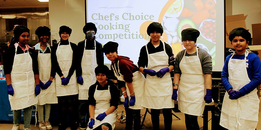 students wearing chef hats and aprons line up before the cooking competition