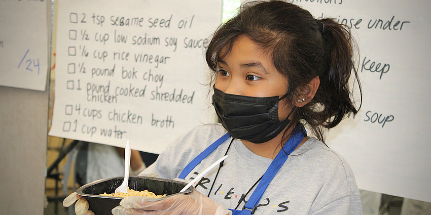 girl with mask and gloves holding a dish of food