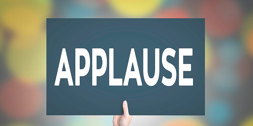 a hand holds up a sign that has the word Applause on it