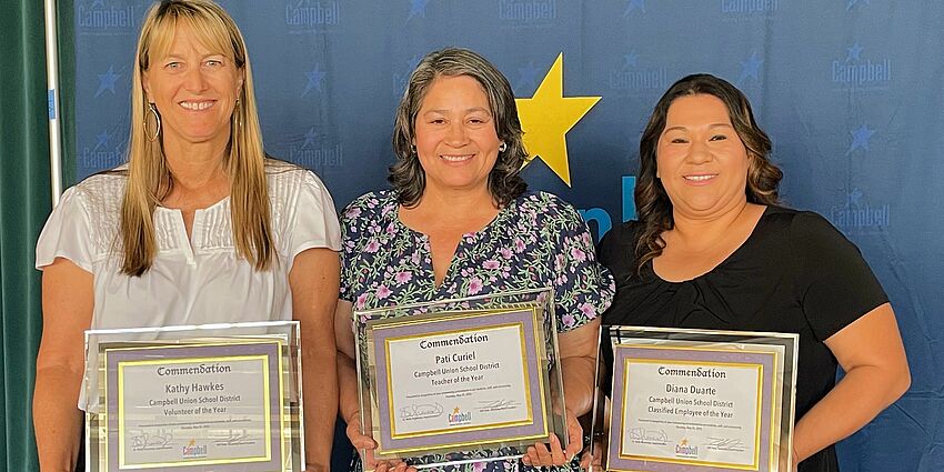 three smiling women holding framed award certificates.