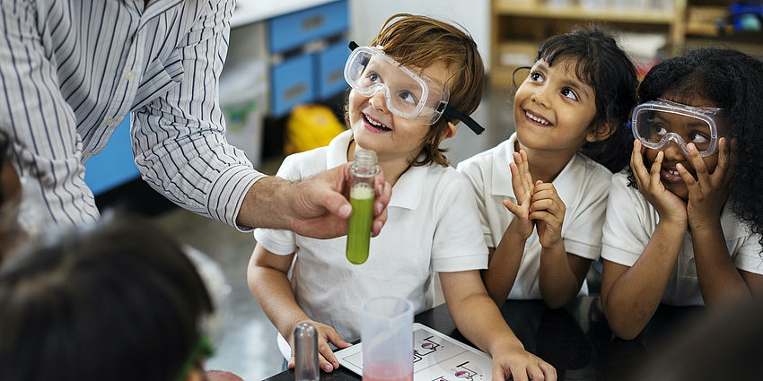 three young students smiling as adult demonstrates experiment