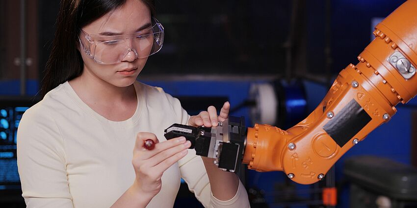 young woman wearing eye protection is fixing the end of a robotic arm