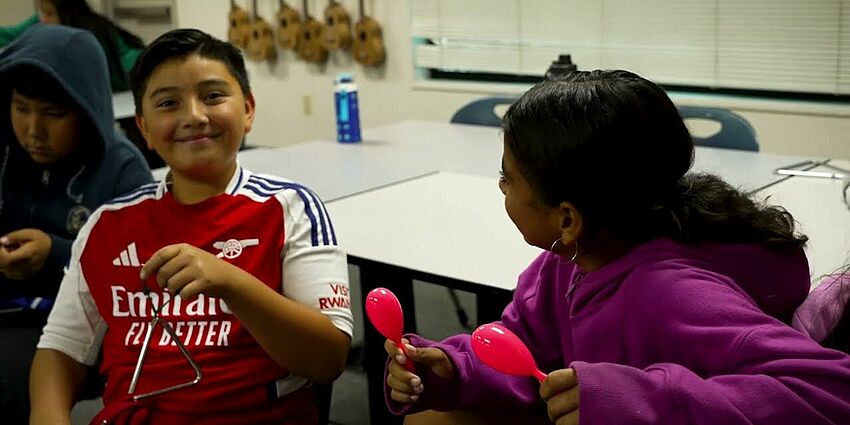 boy smiling and holding a triangle musical instrument.