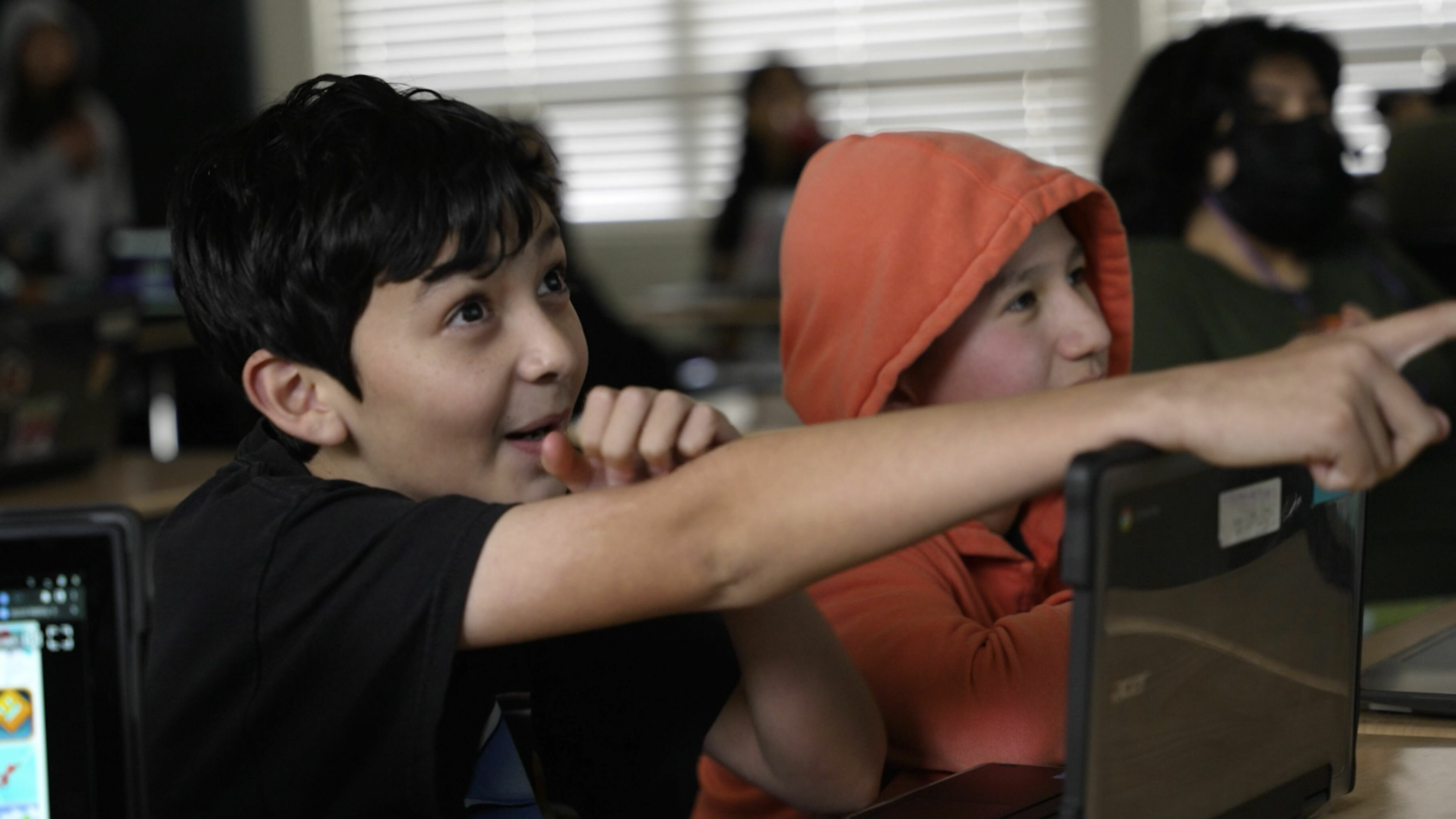 middle school boy at desk looks excited as he points in front of him.