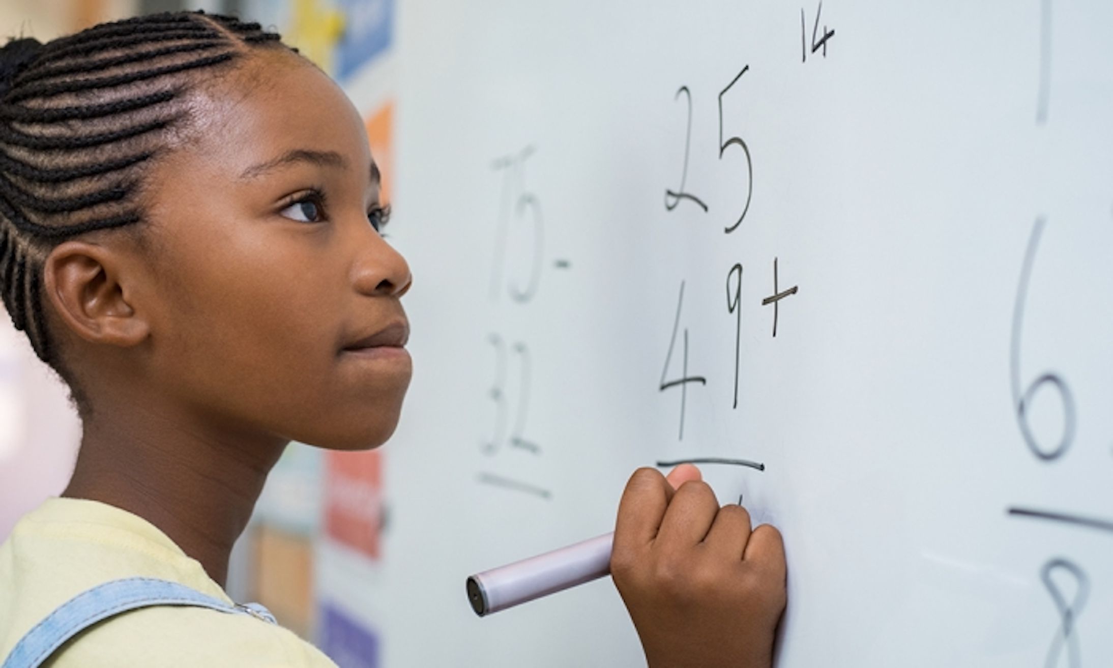 young girl working a math problem on a white board